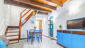A living room with a staircase, a dining table with chairs, a blue cabinet, and a TV.