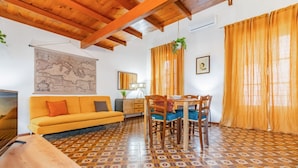 Ein Zimmer mit einem gemusterten Boden, einem Sofa, einem Esstisch mit Stühlen, einer Karte an der Wand und Vorhängen.
