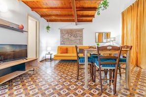 A living room with a TV, sofa, dining table, chairs, and patterned floor tiles.