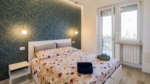 A bedroom with a bed, bedside tables, a window with a view, and a patterned wall. - GuestHost - Waterfront Sea View Modern Apartment with Balcony! (Pescara)