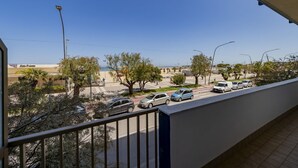 A balcony with a view of a street, cars, trees, and a building with a sign. - GuestHost - Waterfront Sea View Modern Apartment with Balcony! (Pescara)