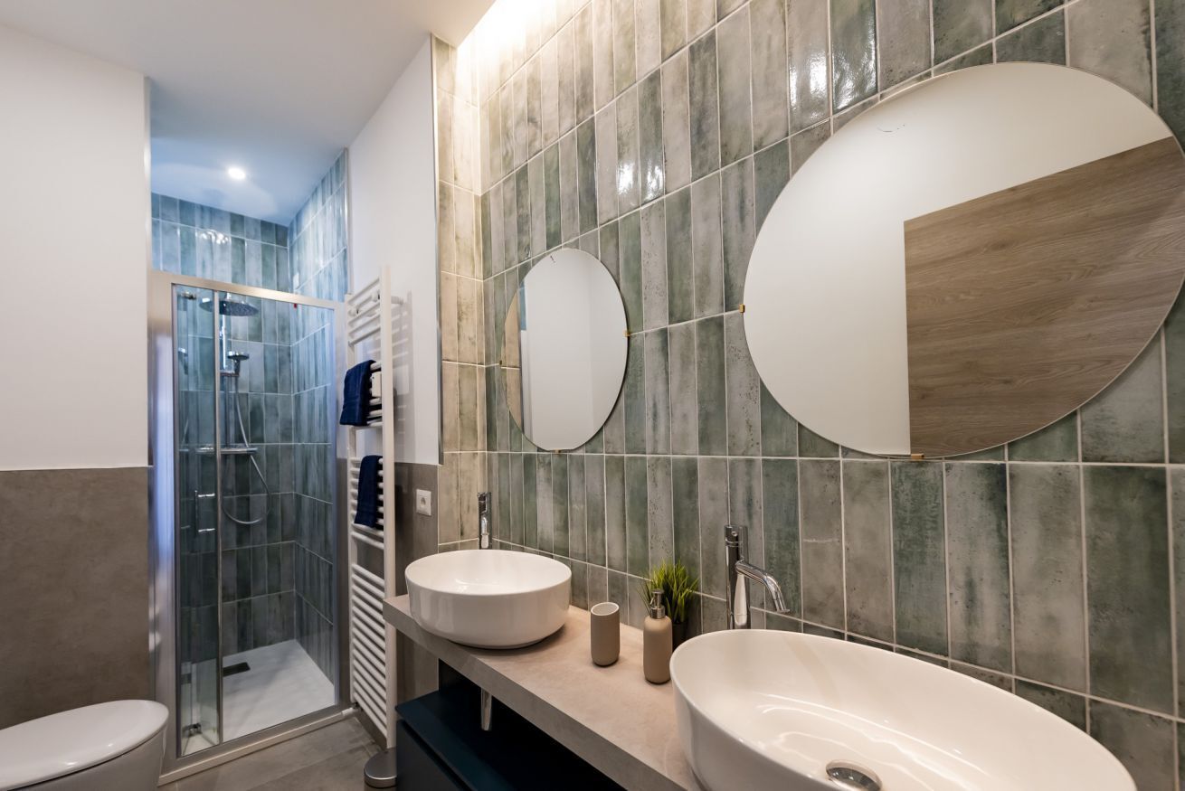 A modern bathroom with a glass shower enclosure, two sinks, and a large mirror.
