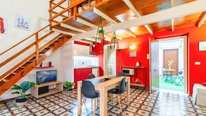 Amplia sala de estar con una escalera de madera, una mesa de comedor con sillas, una zona de cocina y una pared de acento roja.