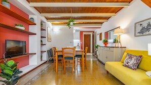 Un comedor con una mesa y sillas de madera, un sofá amarillo y un televisor en la pared.