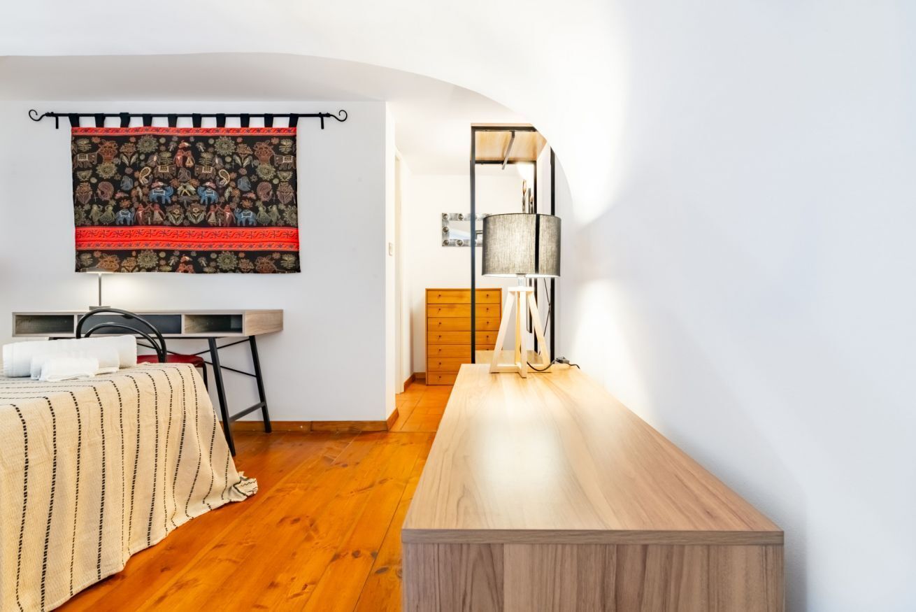 A bedroom with a bed, a desk, a lamp, and a tapestry on the wall.