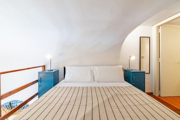 A bedroom with a bed, two bedside tables, a mirror, and a wardrobe.