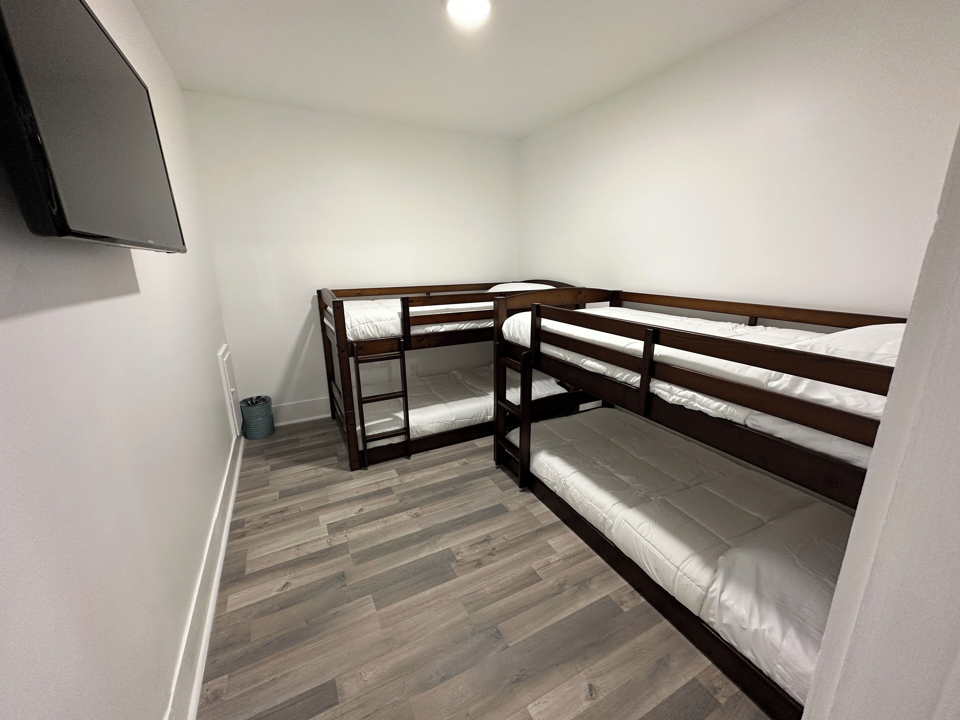 Une chambre avec deux lits superposés, une petite poubelle et un téléviseur fixé au mur.