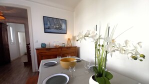 Un coin repas avec une table dressée pour quatre personnes, un grand vase rempli d’orchidées blanches et un tableau encadré accroché au mur.