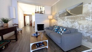 Un salon avec un canapé gris, une table basse et une cheminée. Un escalier mène à l’étage supérieur.