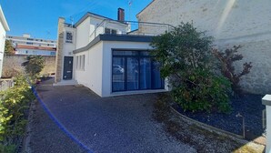 Une maison moderne à deux étages, dotée d’un petit jardin à l’avant et d’une allée gravillonnée.