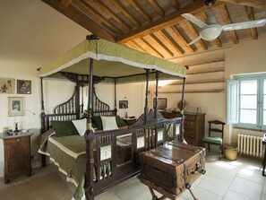 A four-poster canopy bed with a vintage trunk in a room with wooden beams and a ceiling fan. - Belvilla by OYO Villa With Private Pool (San Casciano dei Bagni)