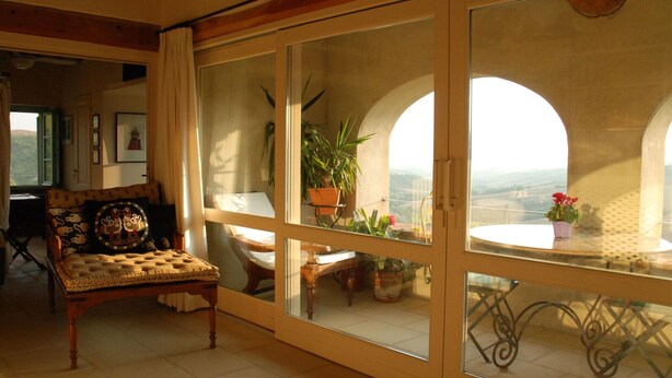 Una habitación acogedora con un ventanal grande, un banco de madera y una mesa con plantas en macetas.
