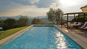 Piscina rectangular con agua cristalina, rodeada por una terraza de madera y sillones de descanso.