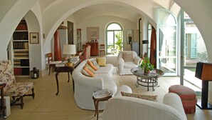 Un salón espacioso con un techo alto abovedado, sofás blancos, una mesa de centro y vistas amplias a través de grandes ventanales.