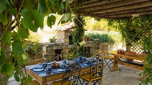 Un espacio de comedor al aire libre con una mesa y sillas de piedra, rodeado de follaje y una chimenea de piedra.