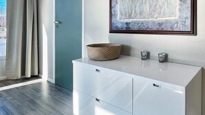 Une pièce moderne avec un meuble blanc, un panier en osier et une œuvre d’art encadrée accrochée au mur.