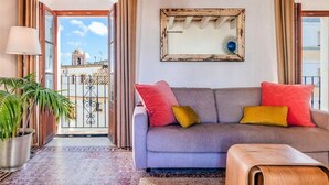 A living room with a grey sofa, red and yellow cushions, a wooden coffee table, a hanging light fixture, and a large mirror on the wall. - Belvilla by OYO Atico 00 (Tarifa)