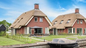 A canal-side house with a boat docked in front, a lawn, and a patio area. - Villa With Garden, in a Holiday Park at the Water (Idskenhuizen)