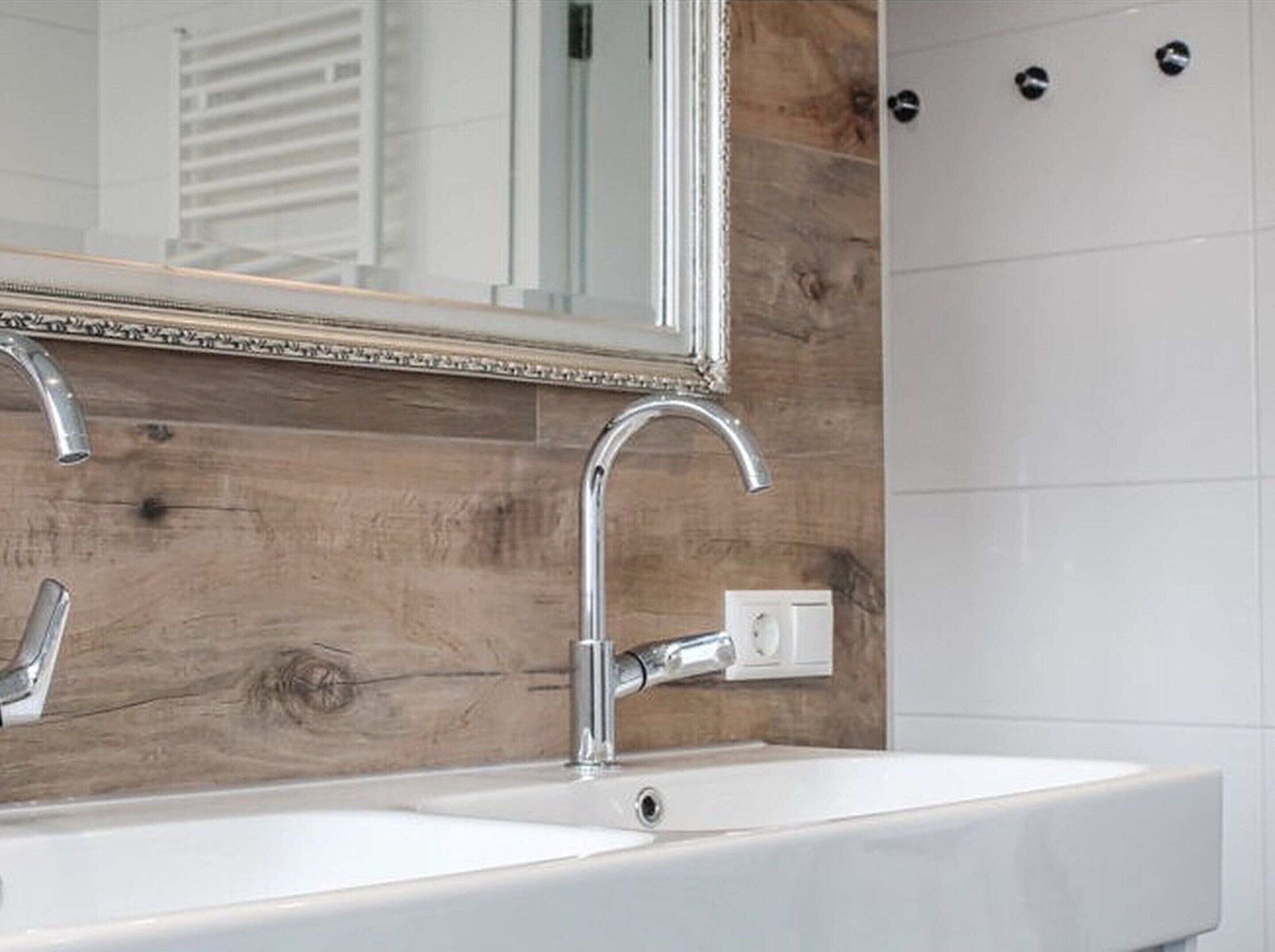 A bathroom with a wooden wall, a white sink, and a mirror with a decorative frame.