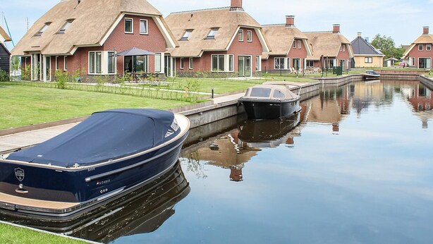 A canal with a row of houses on one side and a boat docked on the other. - Villa With Garden, in a Holiday Park at the Water (Idskenhuizen)