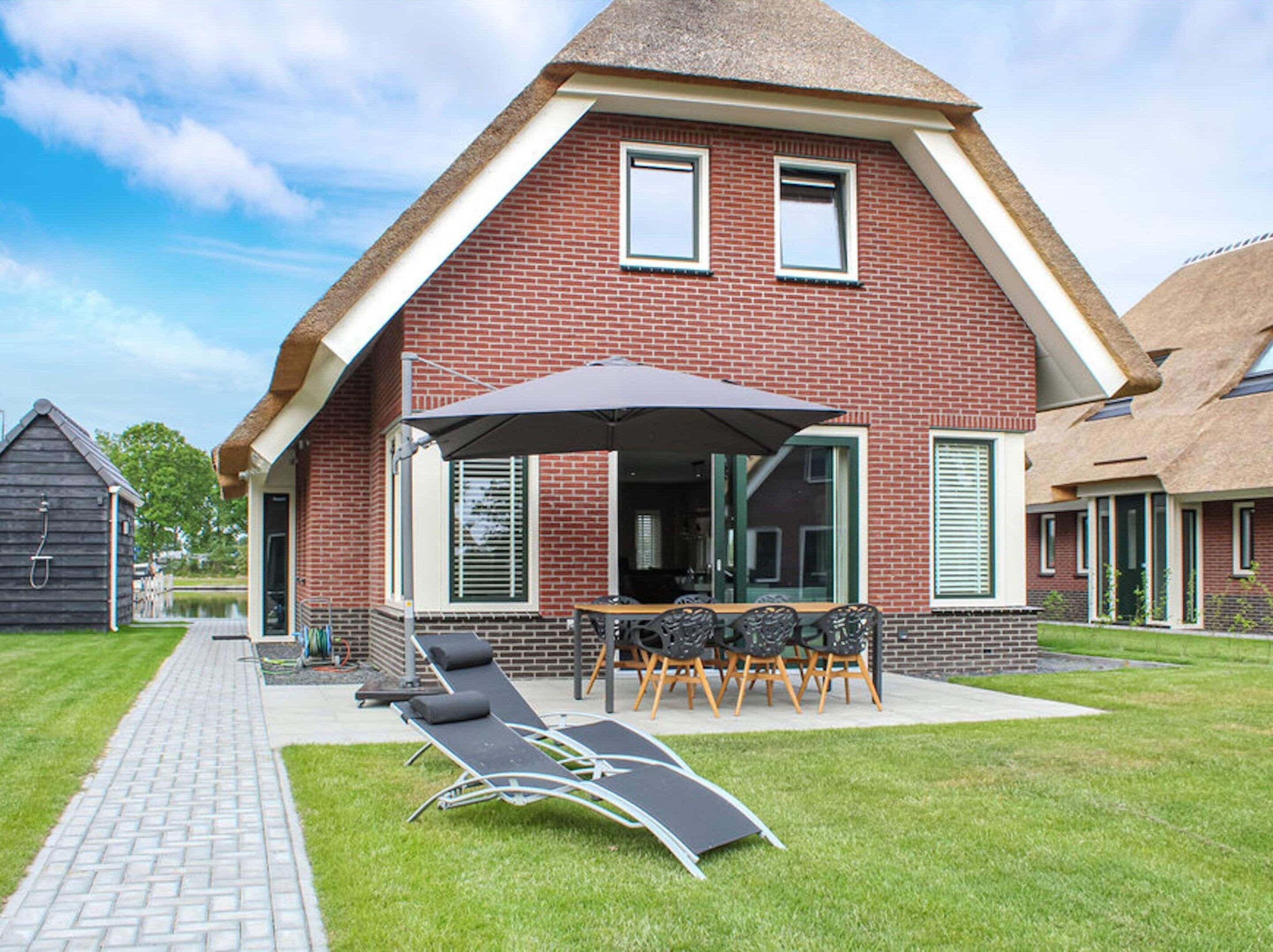 Ein modernes Haus mit Ziegelaußenwand, einer überdachten Terrasse mit Gartenmöbeln und einem Rasen.