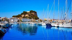 A marina with boats docked, a building with a balcony, and a hill with trees in the background. - Belvilla by OYO Villa Josefina (Denia)