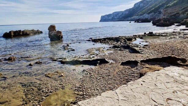 A rocky beach with clear water, a large rock formation, and a distant mountain. - Belvilla by OYO Villa Josefina (Denia)