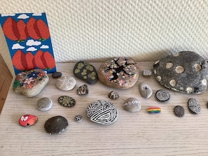 A collection of painted rocks with various designs, including flowers, trees, and abstract patterns, arranged on a wooden surface.