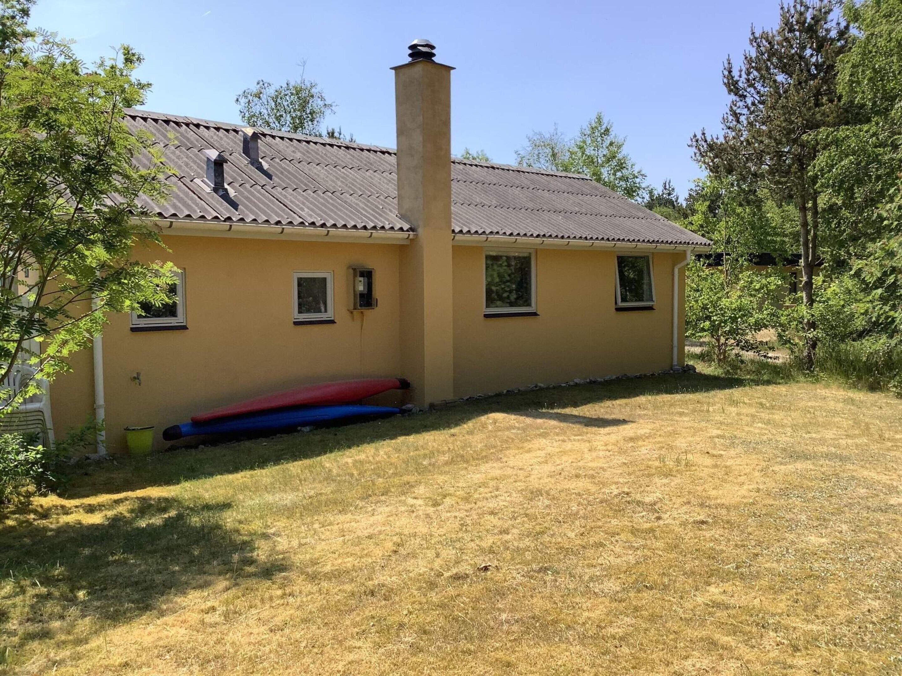 Een laag huis met een gele gevel, een schoorsteen en een klein voortuintje.