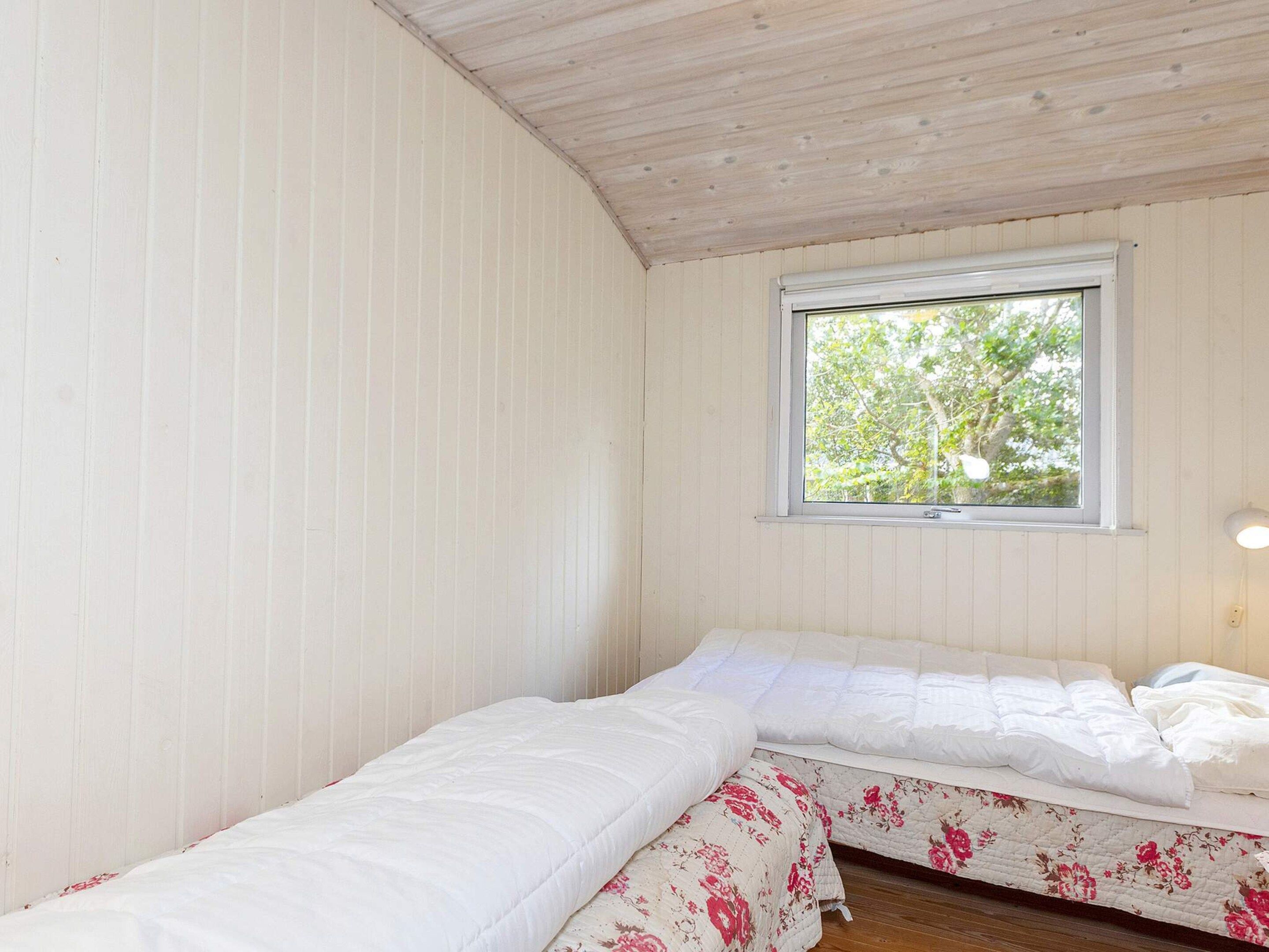 Een kleine, eenvoudige kamer met twee bedden, een raam en een houten plafond.