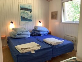 Una habitación con dos camas, cada una con ropa de cama y almohadas azules, un cartel en la pared y una ventana con vistas a árboles.