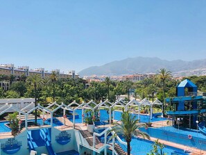 Um resort com várias piscinas, palmeiras e montanhas ao fundo.