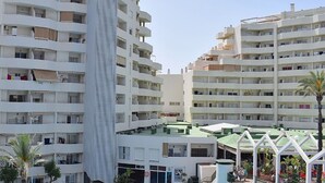 Ένα πολυώροφο ξενοδοχείο με μπαλκόνια, έναν κεντρικό προθάλαμο και μια ταράτσα.