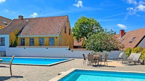 A swimming pool area with tiled roofs, outdoor seating, and a tree. - 2 Person Holiday Home in Gudhjem (Gudhjem)