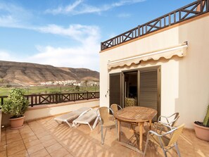 A terrace with a table and chairs, a pair of sun loungers, and a view of a distant town and hills. - Belvilla by OYO Holiday Home in Jandaa (Pajara)