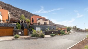 A residential street with houses featuring stone walls and balconies, a clear sky, and a hilly backdrop. - Belvilla by OYO Holiday Home in Jandaa (Pajara)