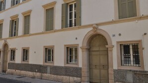 Un immeuble à plusieurs étages, doté d’une façade symétrique, de fenêtres régulièrement espacées et munies de volets, d’une entrée centrale en arc de cercle et d’un socle en pierre.