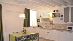 Une cuisine moderne avec des meubles blancs, une table à manger avec des chaises, un luminaire suspendu et une fenêtre avec des rideaux verts.