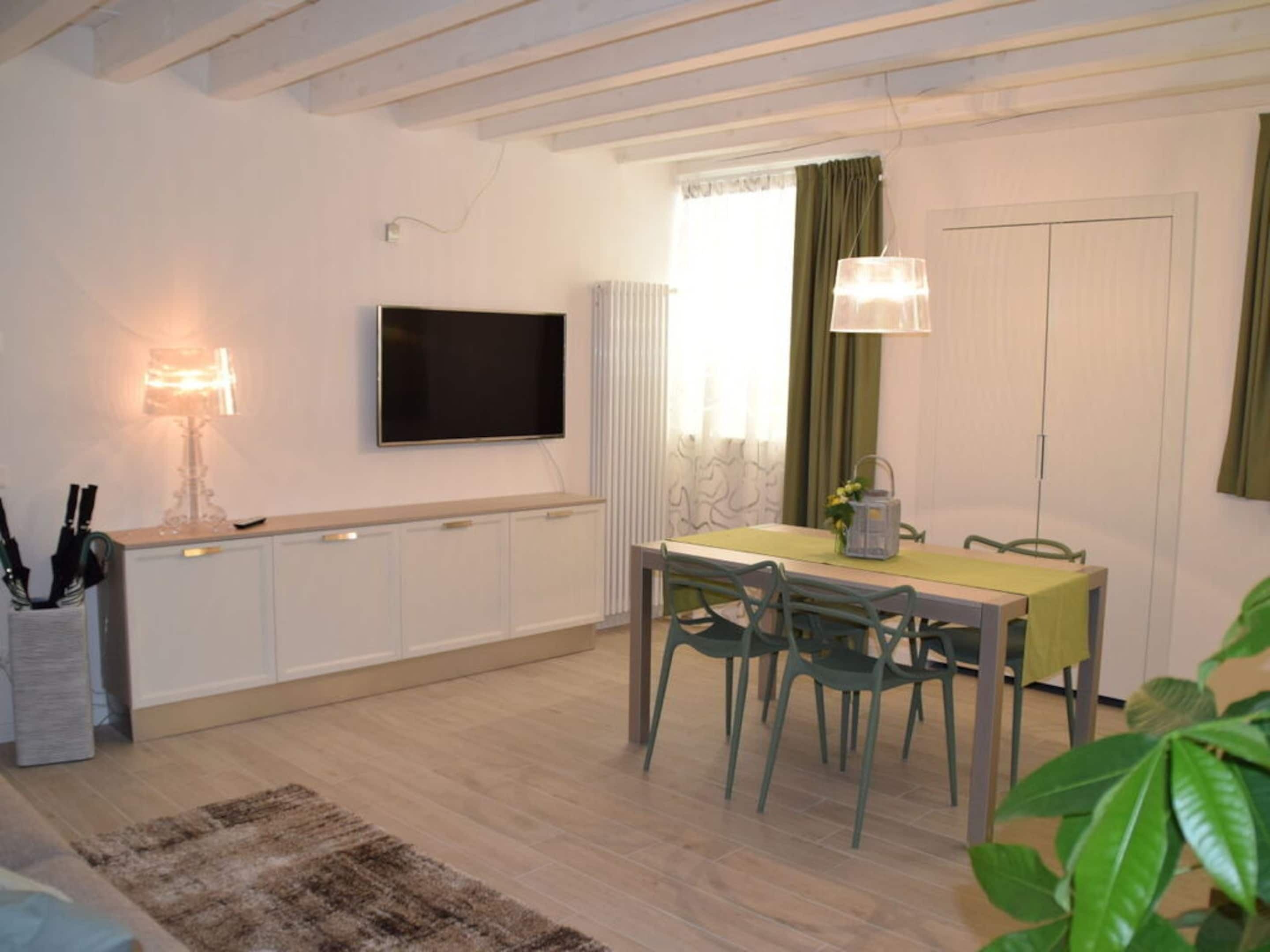 A dining area with a table, chairs, a television mounted on the wall, and a radiator.