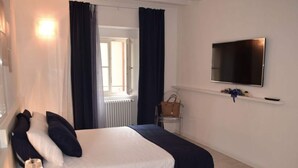 Une chambre bien rangée, avec un lit, un téléviseur fixé au mur, un radiateur et une fenêtre avec des rideaux.