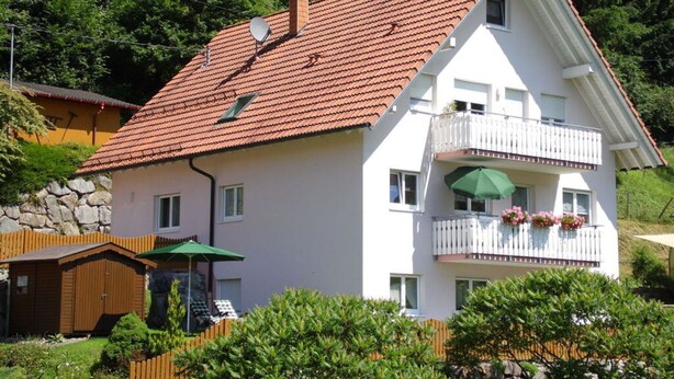 A two-story house with a red-tiled roof, a balcony with a white railing, and a green umbrella. - Am Reichenbach Modern Retreat (Freiamt)