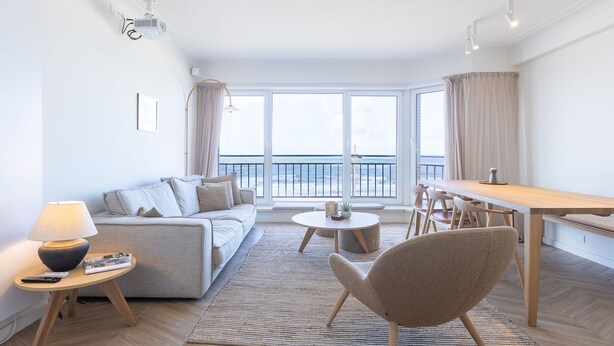 A modern living room with a sofa, a coffee table, and a dining area with a table and chairs. - Bright Apartment With Direct sea View (Middelkerke)