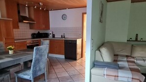 Una cocina con armarios de madera, una mesa de comedor con una silla, un sofá y un reloj en la pared.
