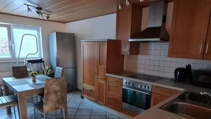 Una cocina con armarios de madera, estufa, refrigerador y un comedor con mesa y sillas.