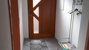 Un pasillo con un tapete estampado, un radiador, una puerta con ventana y un perchero con objetos colgados.