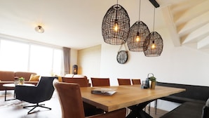 Un espace repas moderne avec une table en bois, des chaises à revêtement marron et des luminaires suspendus.