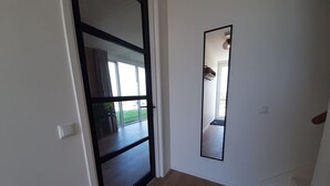 Un couloir avec une porte-fenêtre coulissante donnant sur un balcon, un grand miroir sur le mur et un interrupteur sur le mur.