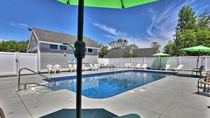 A backyard with a swimming pool, white chairs, and a green umbrella.