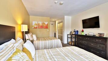 A hotel room with two beds, a TV, a dresser, and artwork on the wall.