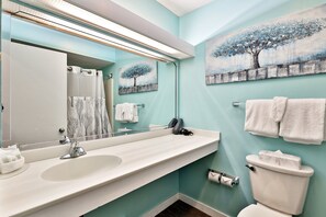 A bathroom with a white sink, a mirror, a toilet, and two paintings on the wall.